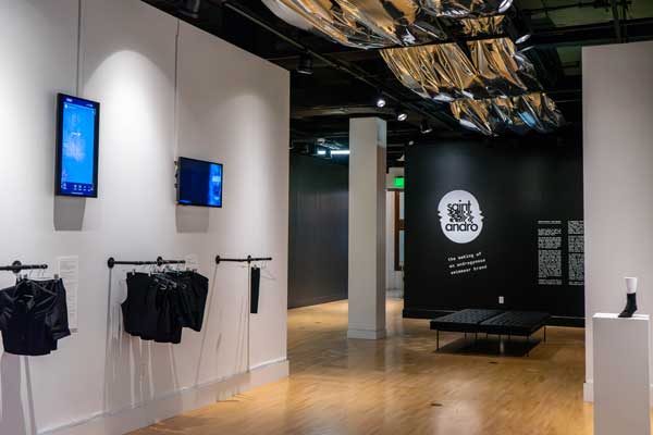 A gallery space with clothes hanging from racks and a plush bench
