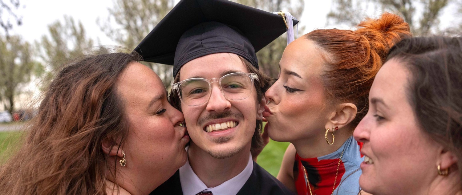 Graduate receiving kisses on the cheek from his family