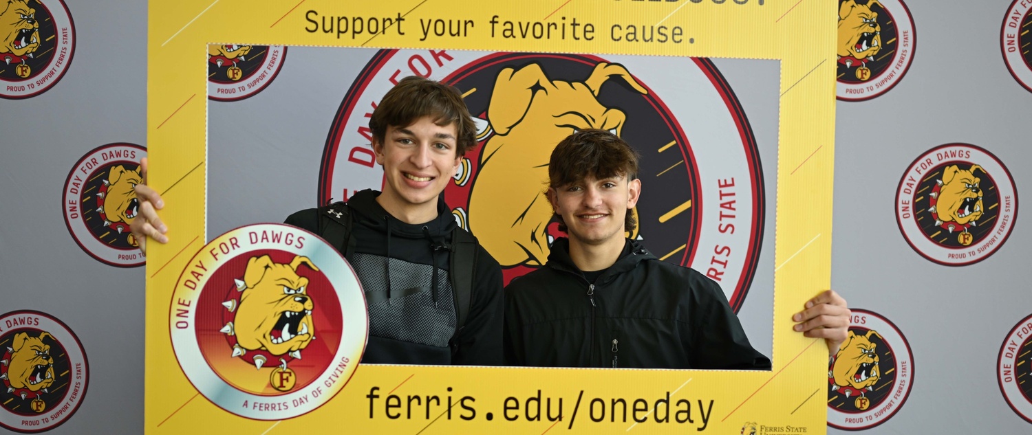 Students posing with a portrait cutout decorated with One Day for Dawgs labels