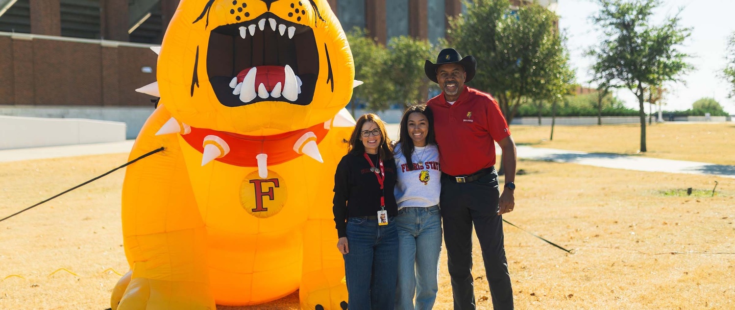 Lori Pink, Ferris State President Bill Pink, and Lydia Pink standing in front of a blow-up Bulldog