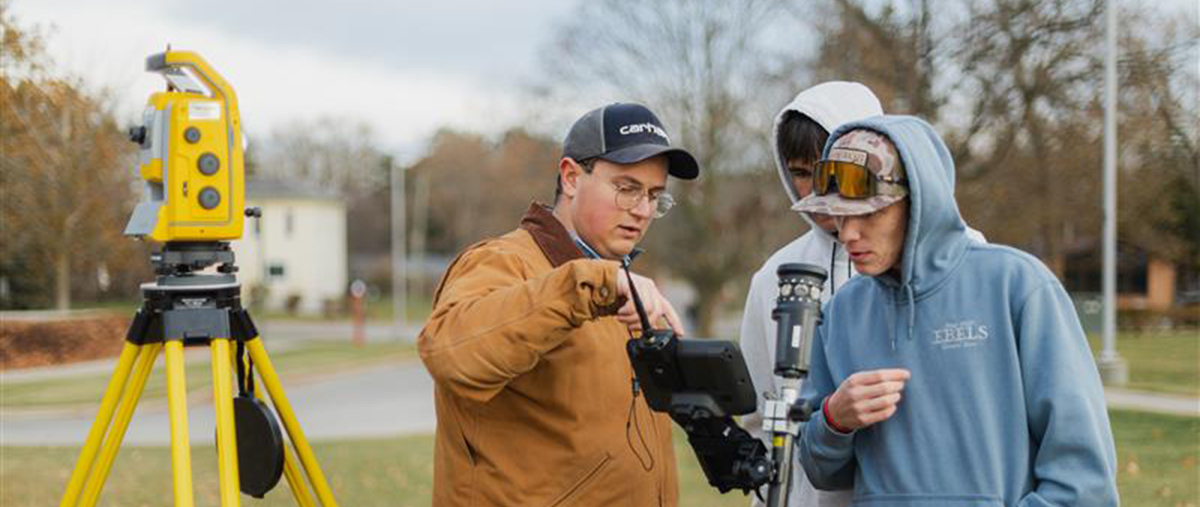 three students using surveying engineering equipment outside